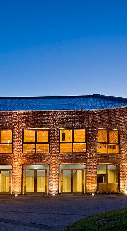 A modern red-brick performing arts building illuminated at dusk, featuring large windows and a geometric design.