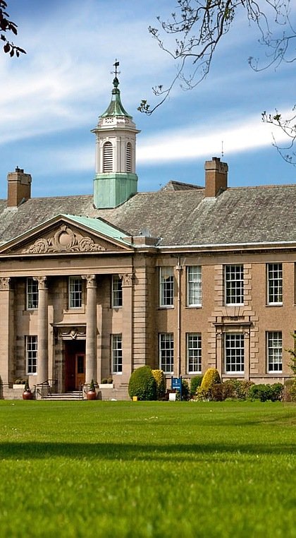 An imposing manor house with trees and green lawns in the foreground