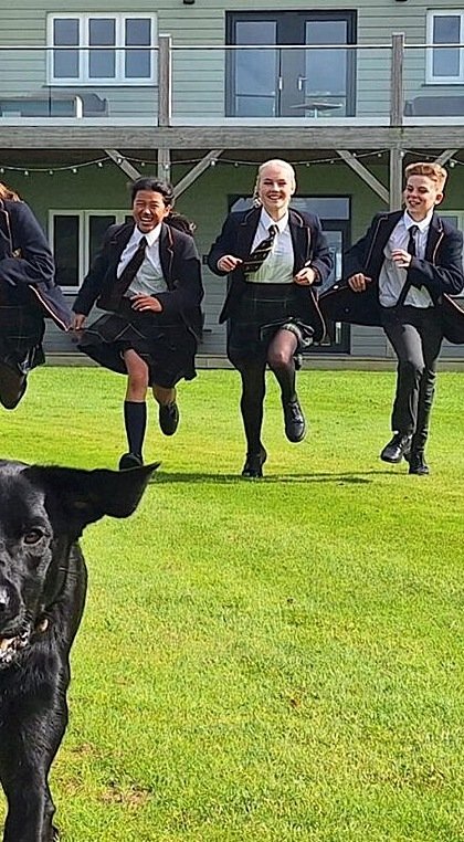 Five children in school uniform running behind a black dog, having fun