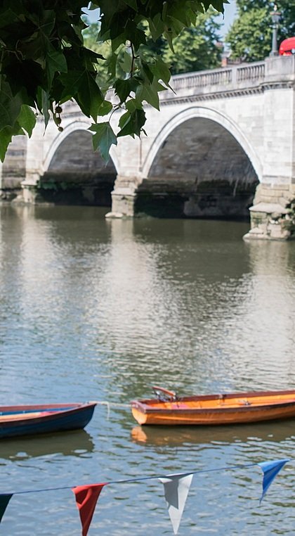 A bridge with round arches across a river with a line of wooden boats lined up