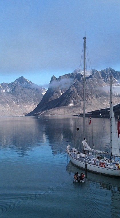 a white two-master in a fjord with snowy mountains in the background