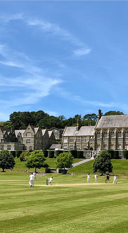 Cricket players on the green outside with the impressive backdrop of Mount Kelly College
