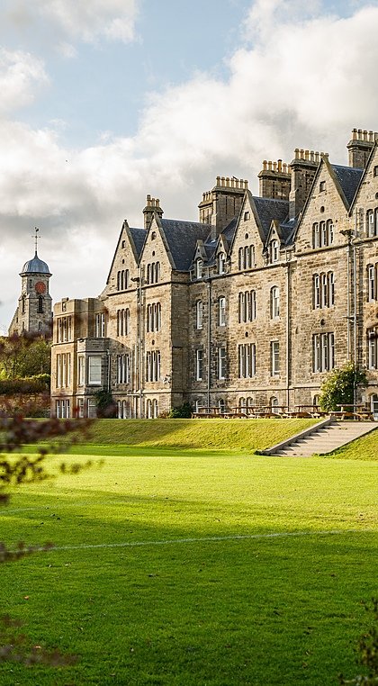 the stunning facade of St Leonards School from the side through bushes on the green campus