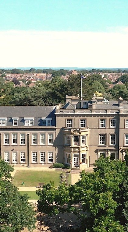 An aerial view of a large historic school building surrounded by trees and residential houses.