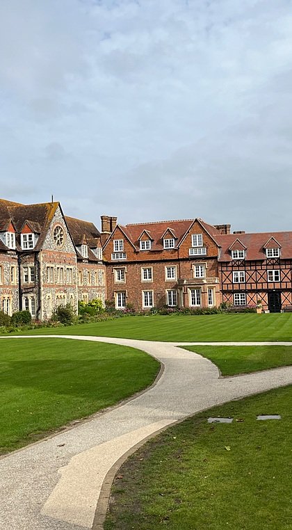 Historic red-brick and stone school buildings surrounding a neatly kept green courtyard.