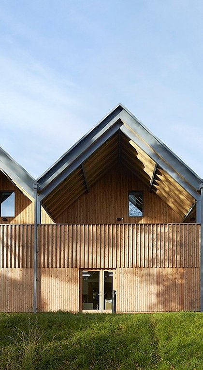 A modern wooden building with a series of steeply gabled roofs and vertical timber cladding in natural light.