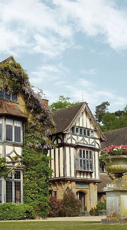 A historic Tudor-style building with ivy-covered walls and gabled roofs surrounded by greenery.
