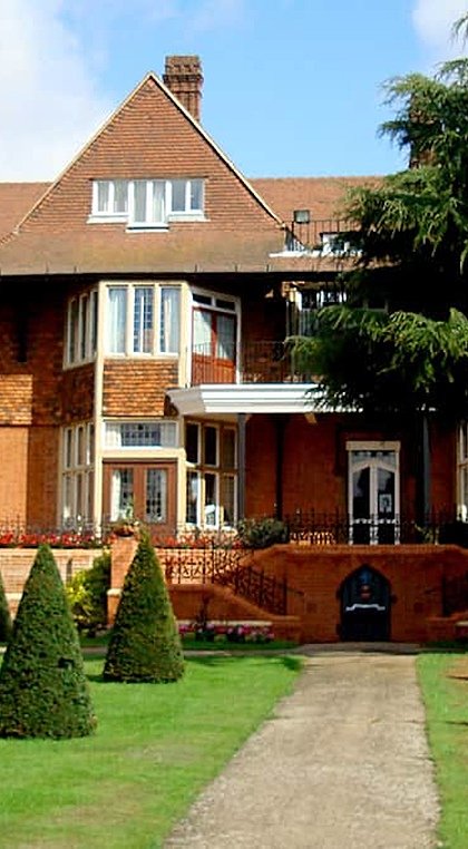 A red brick house with trees and a green lawn in the foreground