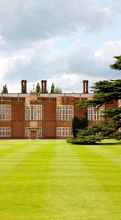 Historic brick school building with a large lawn and mature tree in the foreground.