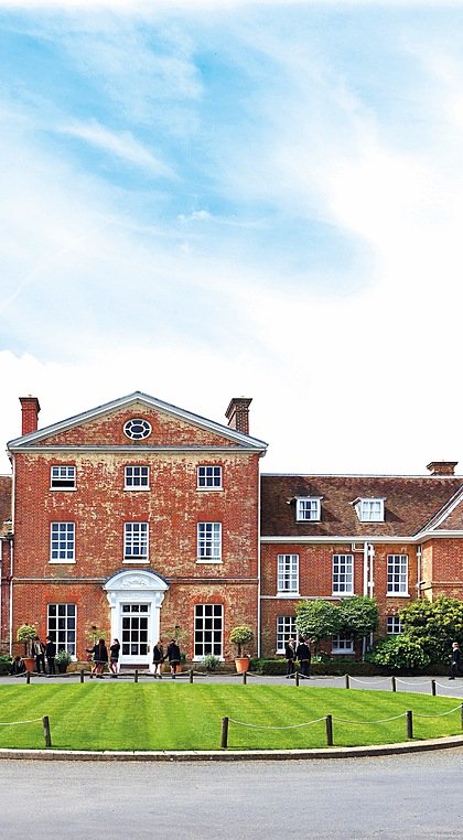 Beautiful red-brick school house with round lawn in front around which pupils walk