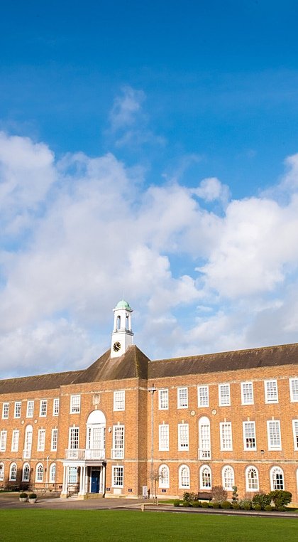 An imposing red brick school building with tower under a blue sky with clouds