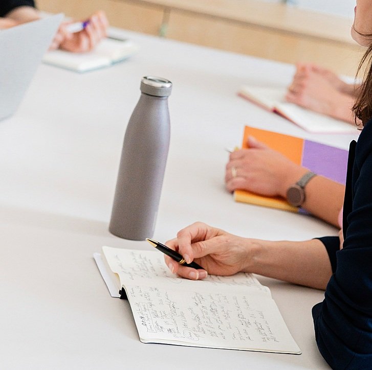 A close-up shot of table, on which a bottle, laptop and hands of people are visible