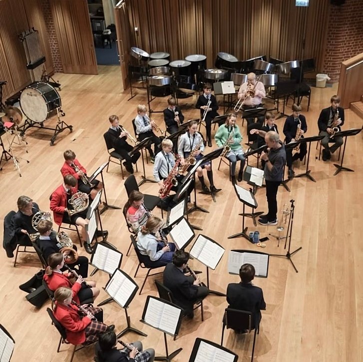 A group of students playing musical instruments in an orchestra rehearsal with a conductor.