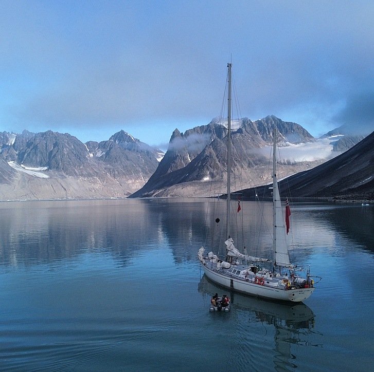 a white two-master in a fjord with snowy mountains in the background