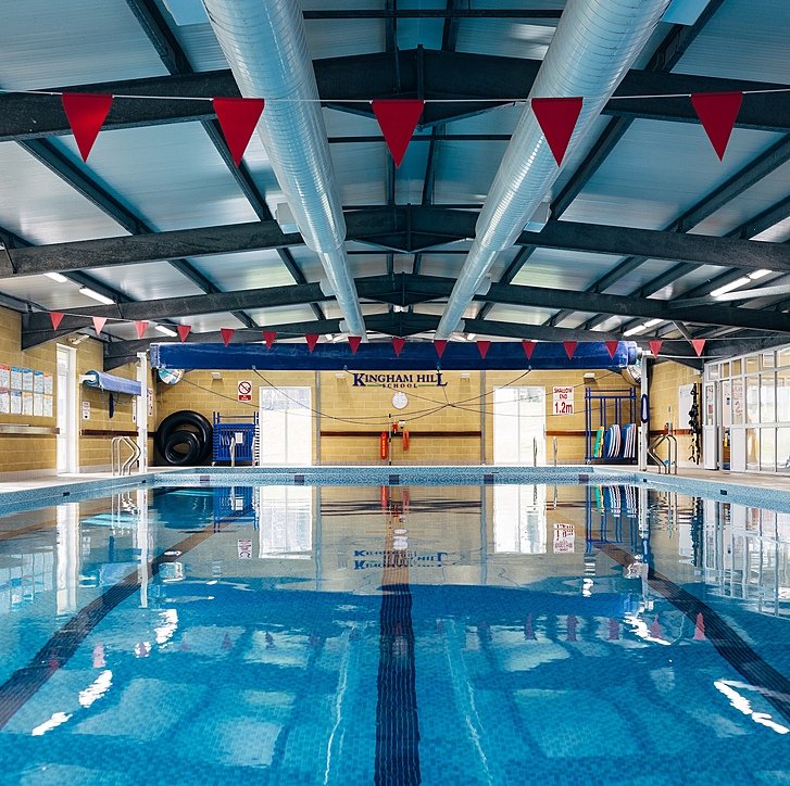 Indoor swimming pool with blue tiles and red triangular flags hanging from the ceiling.