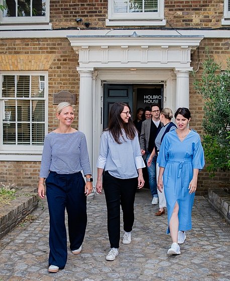 A group of people smiling and walking out of a brick building with a white entrance labeled “Holbrook House.”