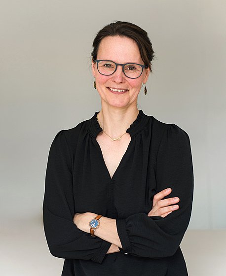 A brunette women with glasses in a black blouse is smiling into the camera