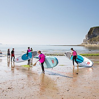 Students carrying their stand up paddle boards across the beach into the water
