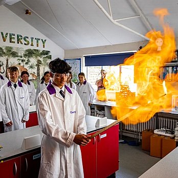 A chemistry student in front and his peers behind him in the science lab is holding a burning stick in front of him