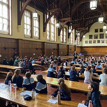Pupils sitting in a large dining hall with wood beams and at large wood tables