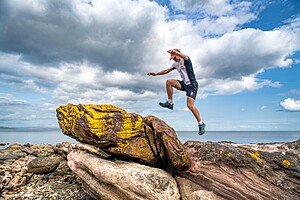 A student jumping over rocks by the sea