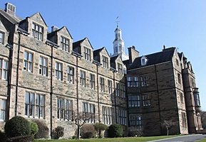 Large traditional stone school building with multiple windows and a white tower.