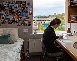Girl sitting at a table in the process of writing with bed in the background