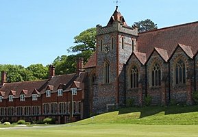 Historic chapel with a clock tower and adjoining red-brick buildings on a sunny day.