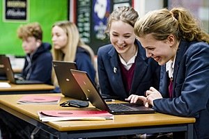 Two girls in school uniform looking at a laptop schreen, smiling