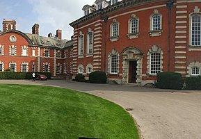 Red-brick institutional building with white stone detailing and arched windows bordering a circular driveway.