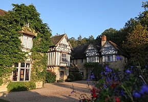 Ivy-covered Tudor-style building with leaded windows and flowerbeds in front.