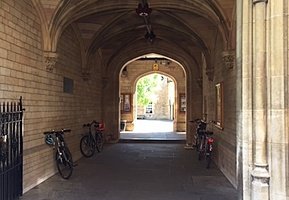 Arched stone passageway with vaulted ceilings and bicycles parked along the walls leading to a bright courtyard.