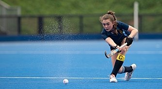 A girl hits the Hockey ball with her stick outside on a blue pitch