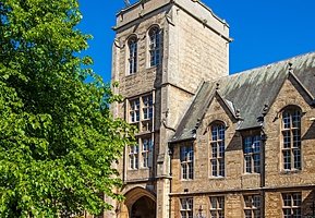 An old school building with a tower and a tree