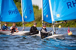 Pupils sailing small boats with bright blue sails on a calm lake, concentrating as they steer and adjust their ropes.