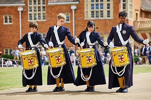 Students in uniform drumming during a school parade performance.