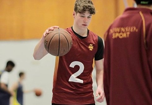 A student wearing a maroon sports jersey dribbling a basketball during practice.