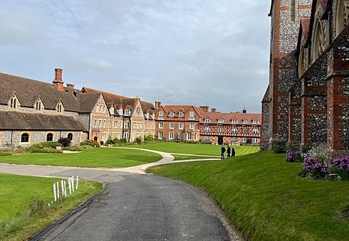 Expansive school grounds with red-brick and flint buildings surrounding a neatly mowed lawn under a cloudy sky.