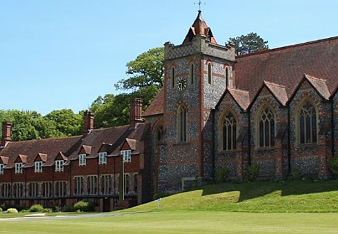 Historic chapel with a clock tower and adjoining red-brick buildings on a sunny day.