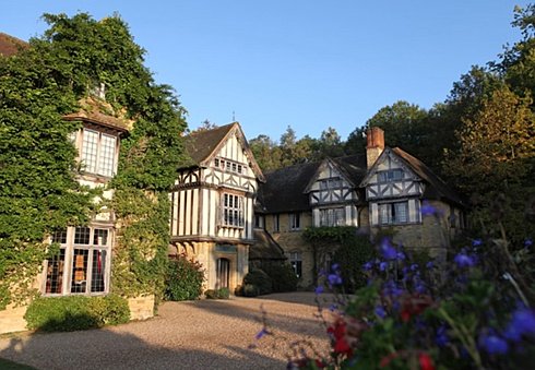 Ivy-covered Tudor-style building with leaded windows and flowerbeds in front.