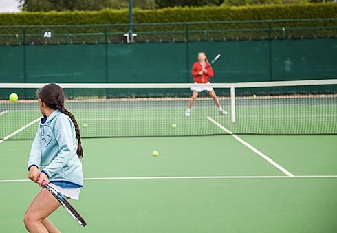 Two students playing tennis on a green court, one preparing to hit the ball.