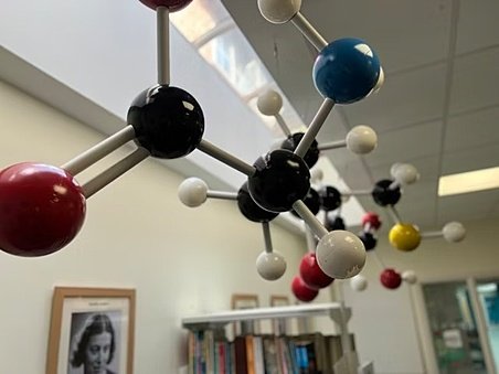 Close-up of a colorful molecular model hanging in a science classroom with bookshelves in the background.