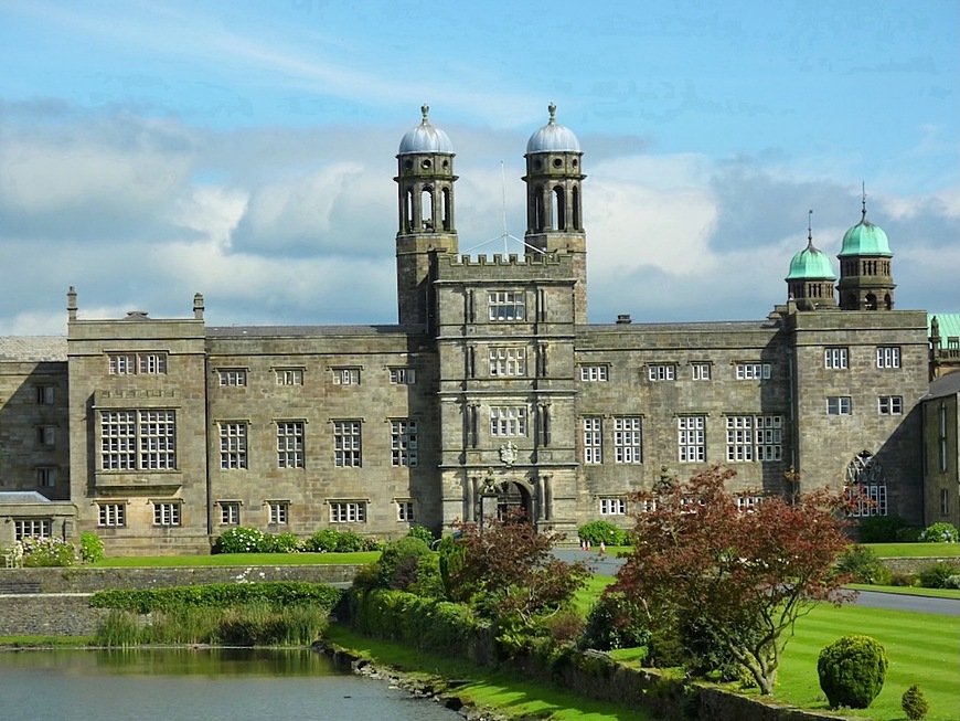 A large historic stone building with twin domed towers, surrounded by landscaped gardens and a reflecting pond.