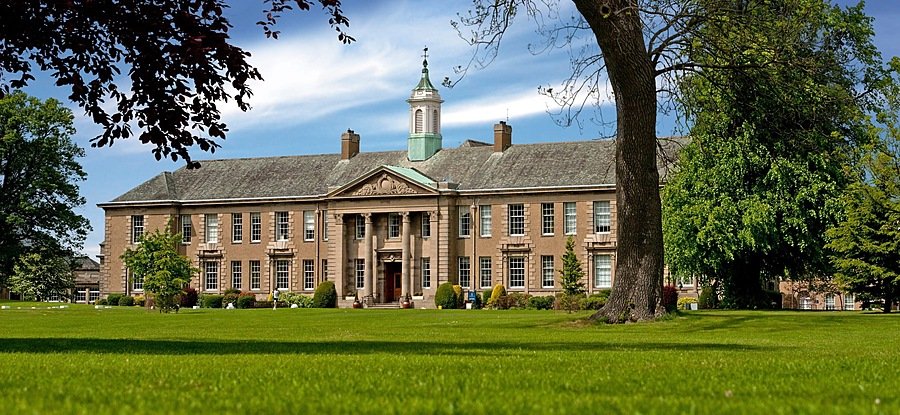 An imposing manor house with trees and green lawns in the foreground