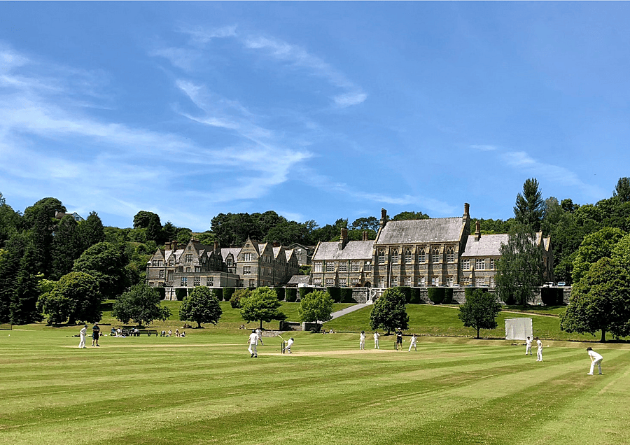 Cricket players on the green outside with the impressive backdrop of Mount Kelly College