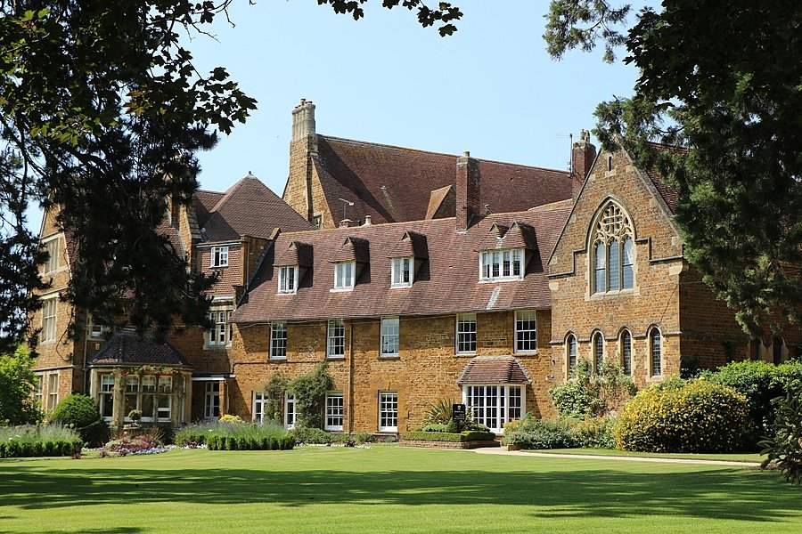 A historic brick building with gabled roofs surrounded by trees and a well-kept lawn.