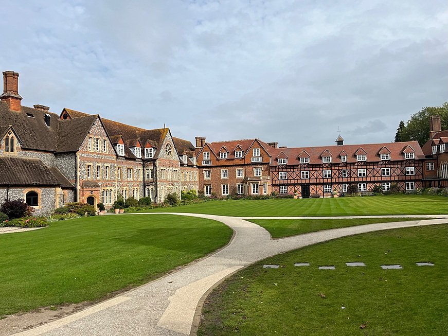Historic red-brick and stone school buildings surrounding a neatly kept green courtyard.
