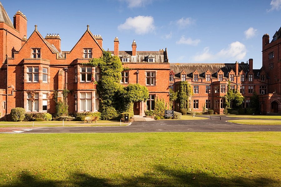 A red-brick school building with ivy-covered walls and large windows, set around a courtyard with green lawns.