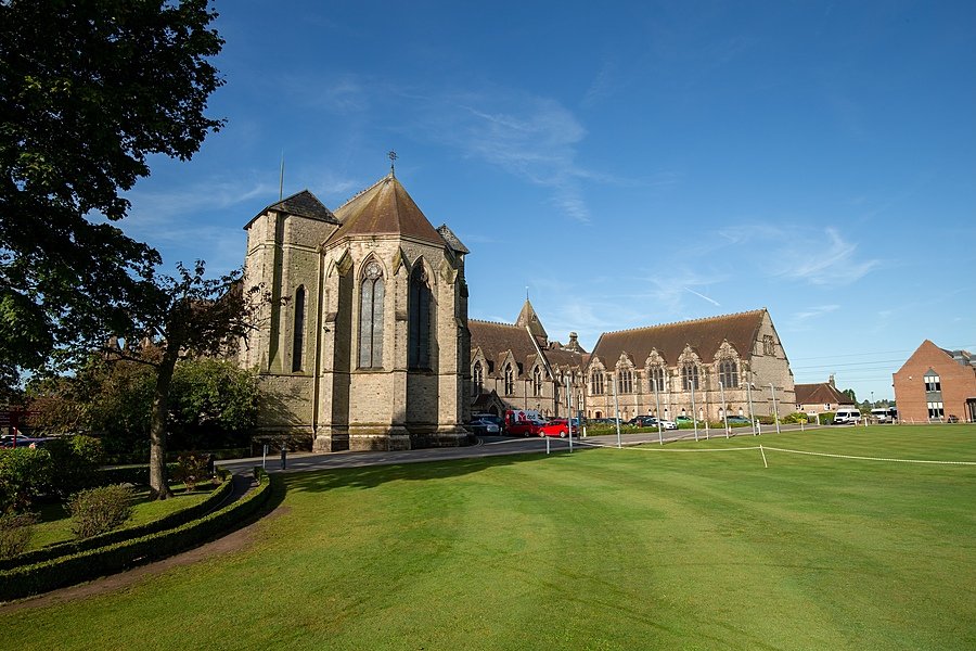 A grand stone chapel and adjoining school buildings set beside a neatly kept lawn under a clear blue sky.