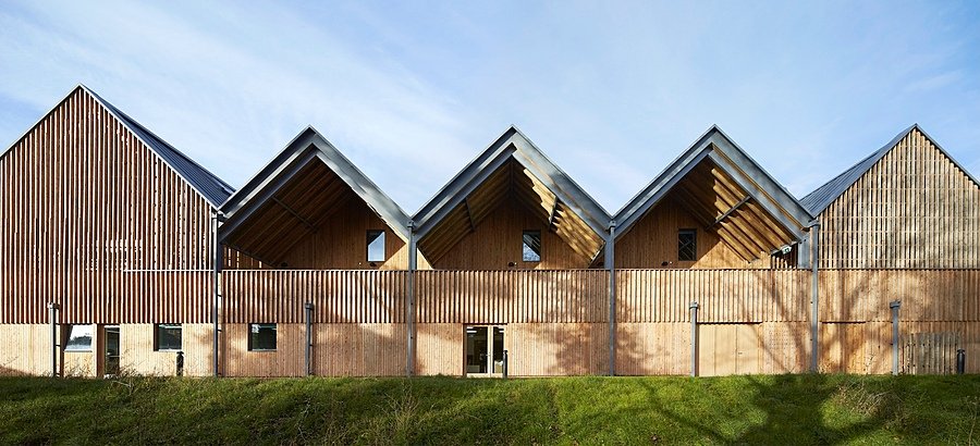 A modern wooden building with a series of steeply gabled roofs and vertical timber cladding in natural light.